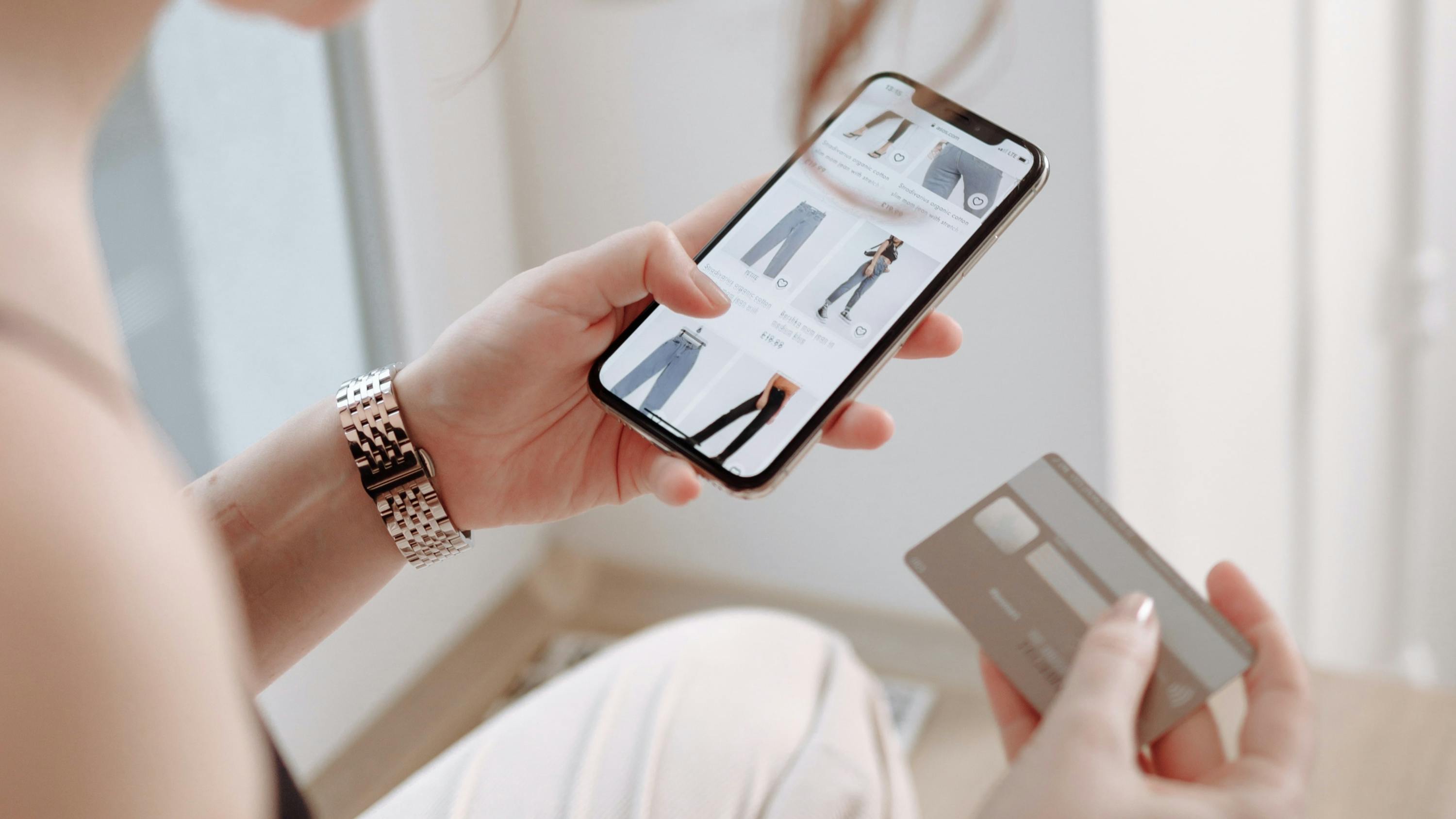 Woman shopping for pants on her smartphone with credit card in other hand