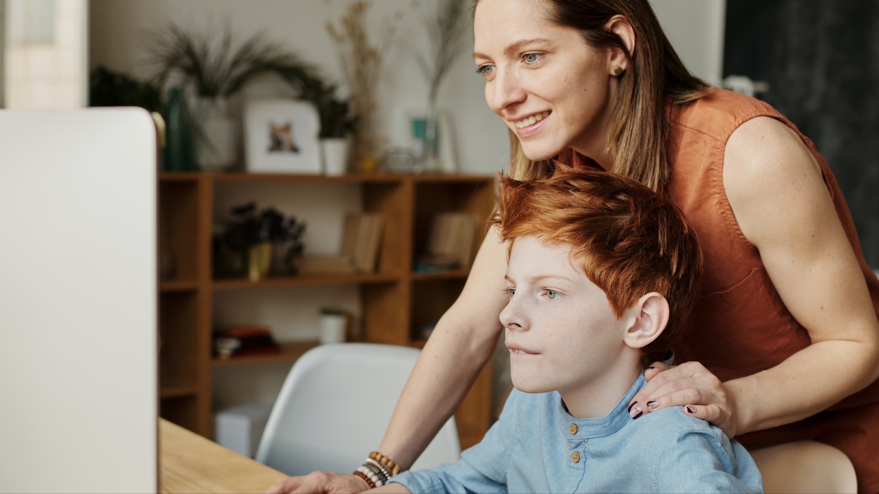 Boy sitting at a computer with his mom behind him looking over his shoulder