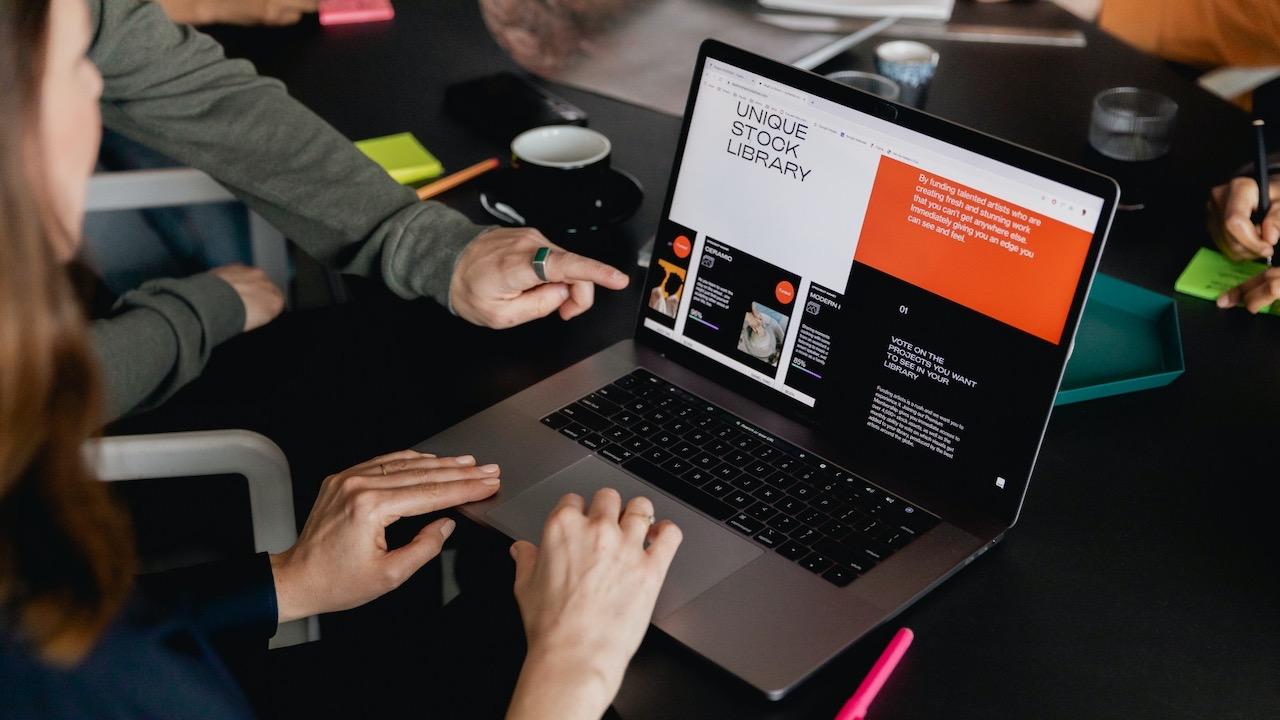 Someone pointing at a laptop screen on a work desk