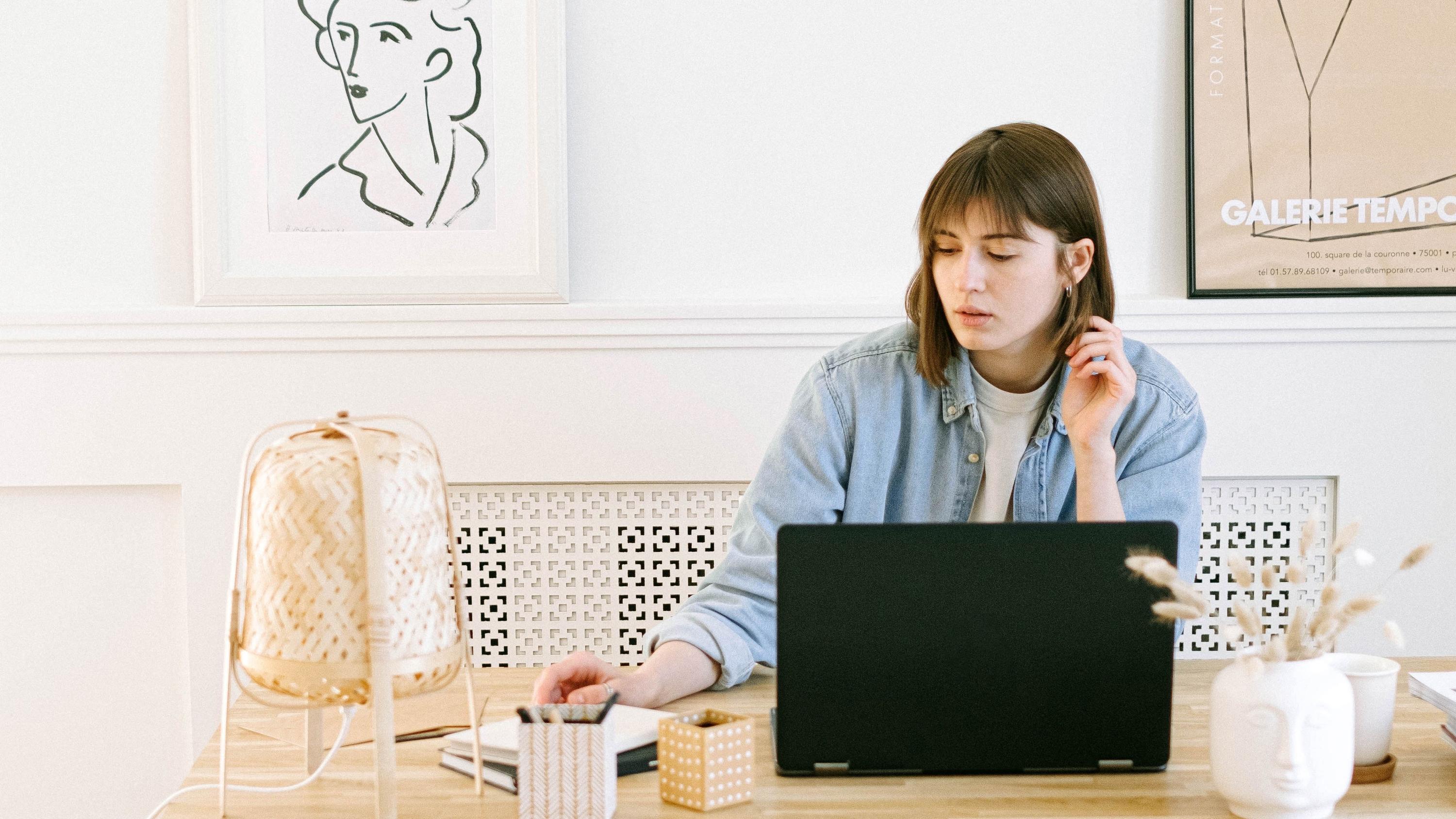 Woman on her laptop at a wooden desk with artwork behind her